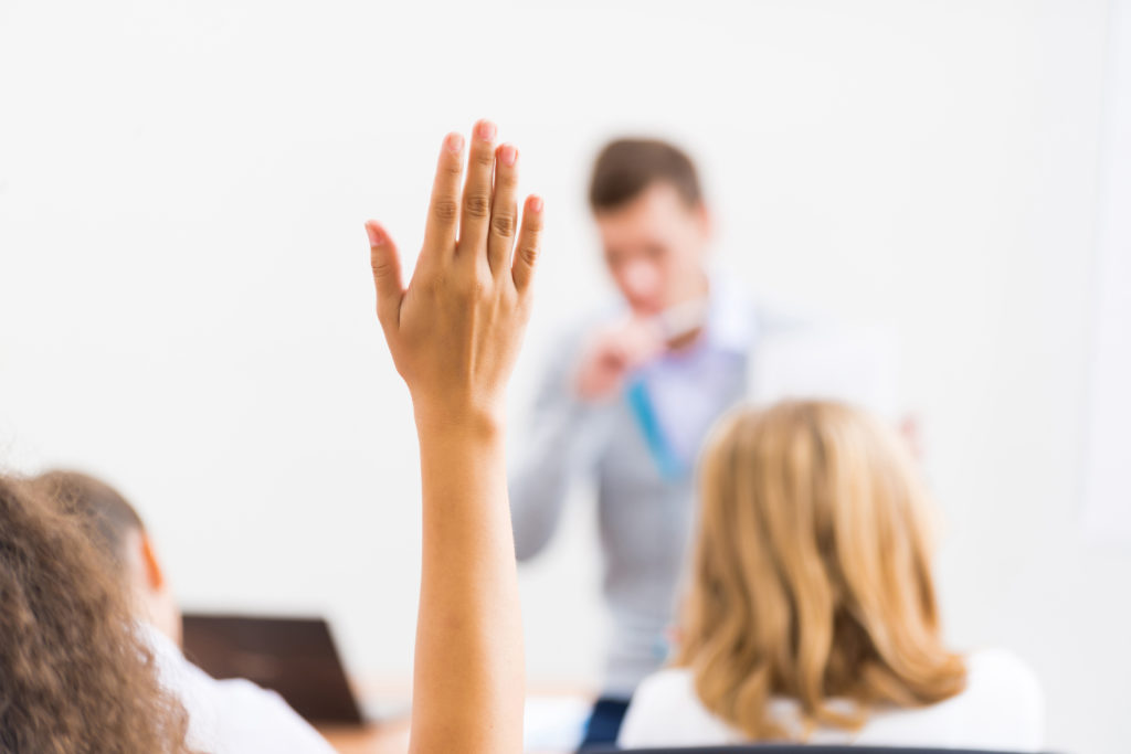 Person raising hand to ask a question in classroom.