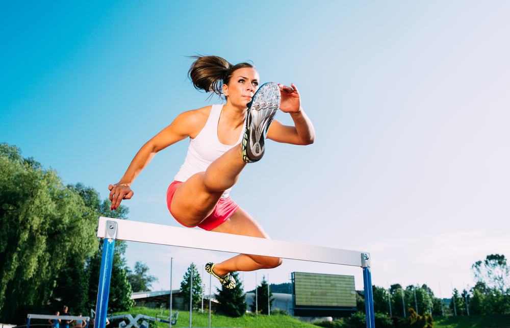 Female athlete jumping over a hurdle.