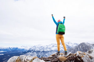 A woman raises her hands in the air on a mountaintop in celebration