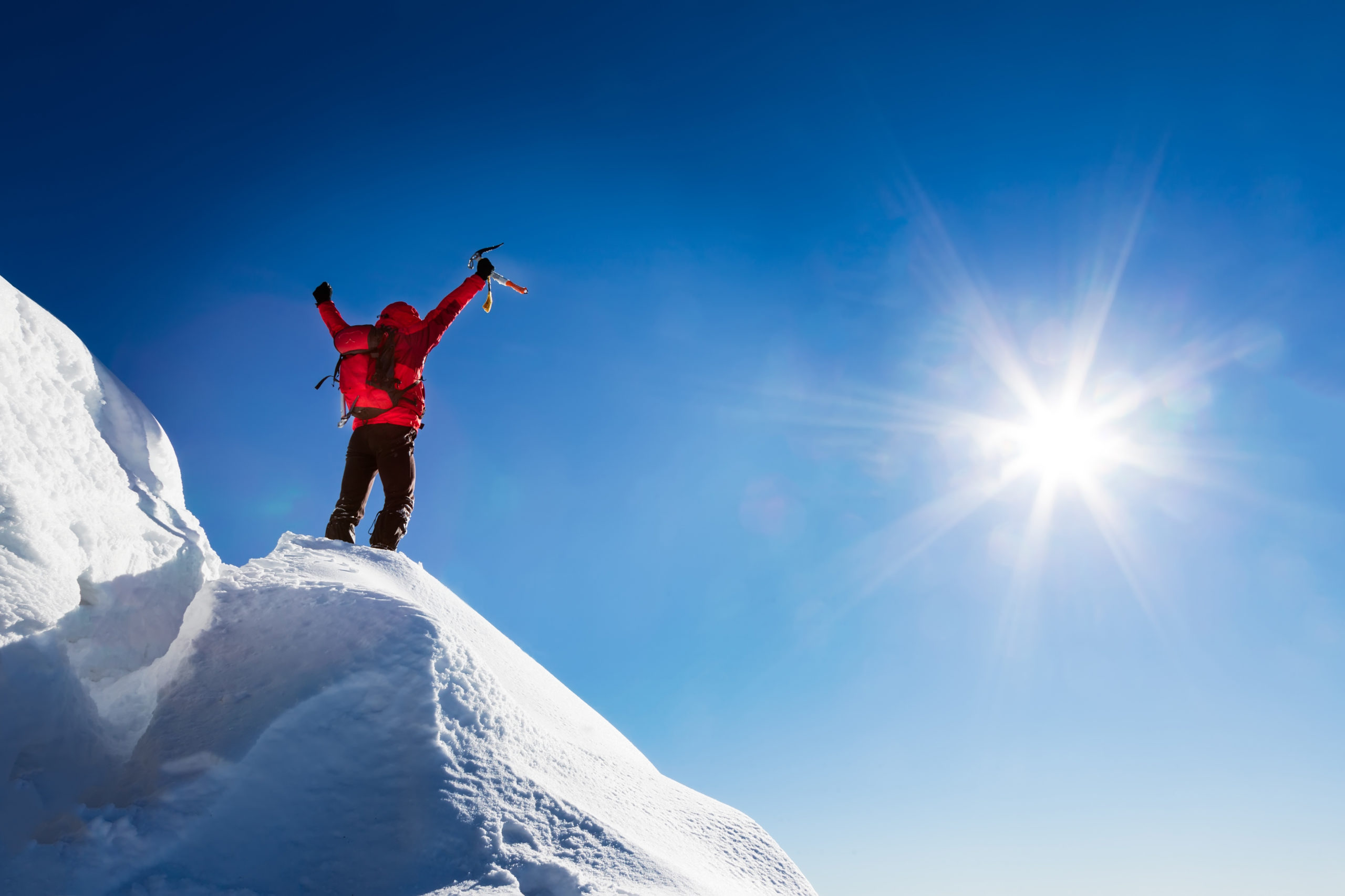 Person in snow gear with backpack standing on snowy peak raising arms in triumph.